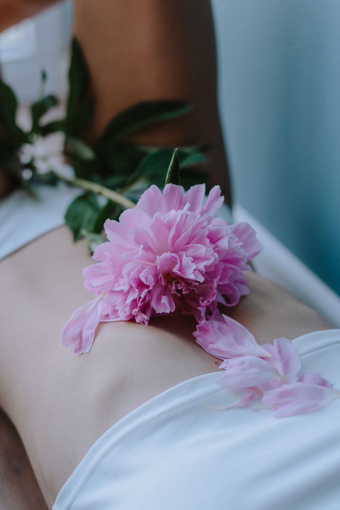 Mastering the First Impression: Your intriguing post title goes here Pink peony flower placed on a woman's abdomen, showcasing natural beauty and tranquility.